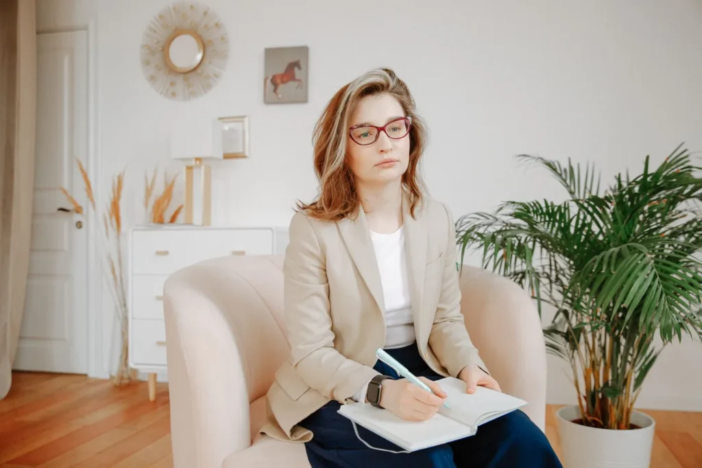 A female therapist in a beige blazer taking notes, focused during a session in a calm office setting