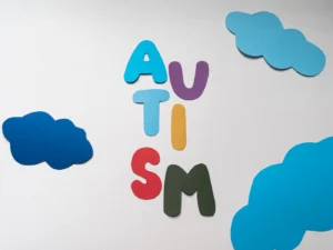 Colorful paper cutouts spelling 'autism' amidst clouds on white background for autism awareness