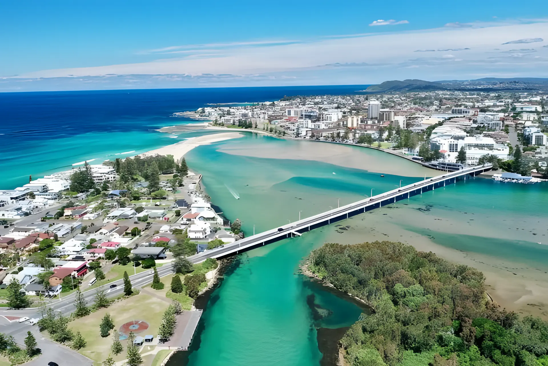 Aerial view of a Central Coast NSW coastal town, with a bridge crossing a turquoise lake channel beside the beach and ocean