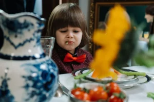 A young child with a humorous expression while eating vegetables at a dining table