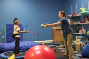Therapist tossing a ball to a child wearing ear defenders in the Real Therapy Solutions sensory gym
