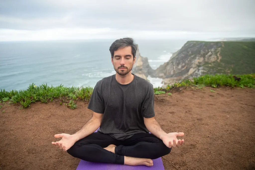 A man meditates on a cliff in Portugal, embracing calmness and nature