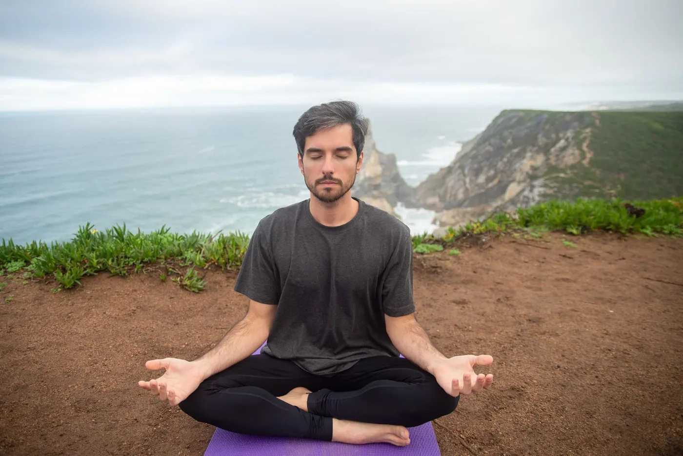 A man meditates on a cliff in Portugal, embracing calmness and nature