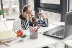 A child wearing headphones doing homework on a laptop indoors. Remote learning setup