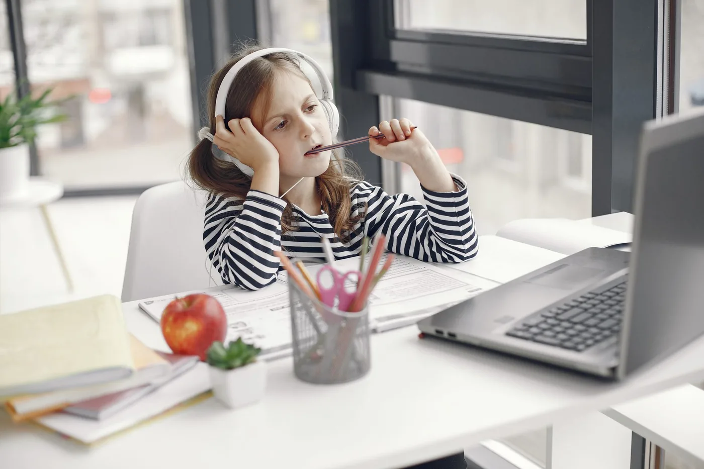 A child wearing headphones doing homework on a laptop indoors. Remote learning setup