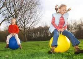 Two children bouncing on space hoppers in a field
