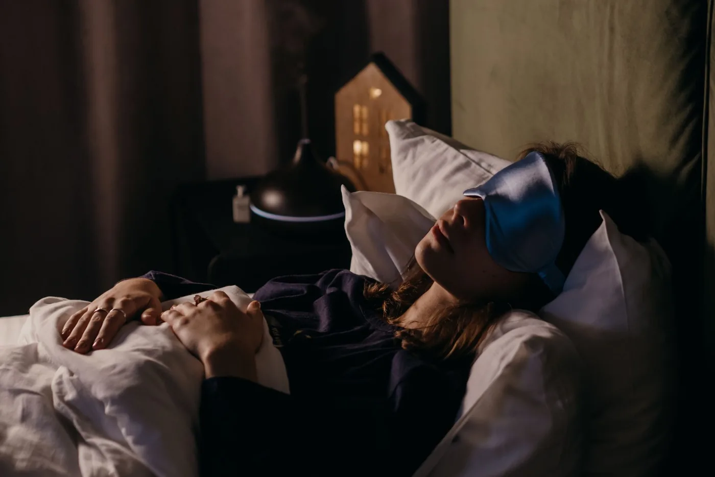 A woman resting with a sleep mask in a calm bedroom setting, creating a serene and cozy atmosphere