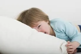 A child lying awake in bed under a duvet