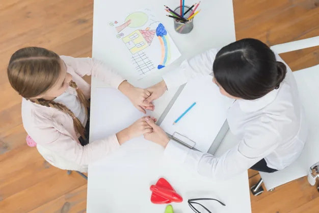 Overhead view little girl female psychologist holding each other s hand white table