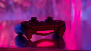 A wireless game controller in focus with a vibrant pink and purple neon background