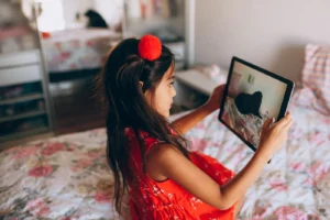 Child in red dress using a tablet in a cozy bedroom. Capturing tech interaction