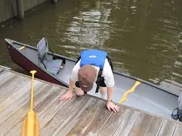 A baby in a life jacket crawling along a jetty beside a canoe