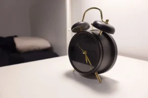 Vintage-style black alarm clock on modern minimalist bedside table in a cozy bedroom