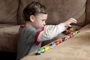 A boy lining up toy cars in a row on the floor