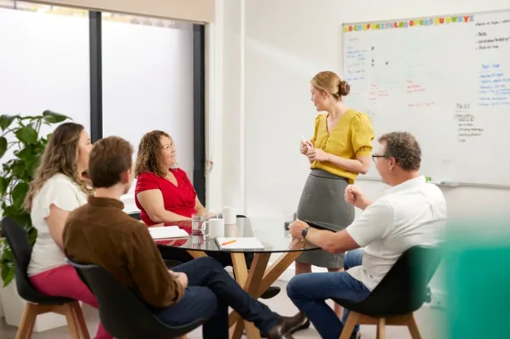 Therapist presenting to a group of support workers seated around a meeting table