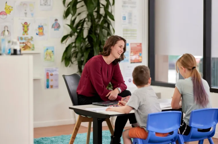 Therapist smiling while working with two children at a table in a Real Therapy Solutions clinic